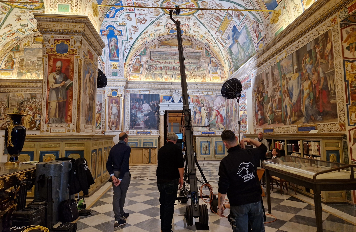 Professional audiovisual production services in Italy - Film crew operating a camera crane and cinema lighting setup inside a historic frescoed hall for an international documentary production in Rome and the Vatican area.