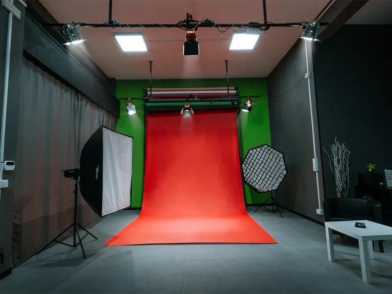 Fully equipped professional video production studio rental in Rome, Italy, featuring a red seamless paper limbo backdrop over a green screen chroma key wall, an overhead ceiling lighting grid, and floor softboxes setup for interviews and podcasts.