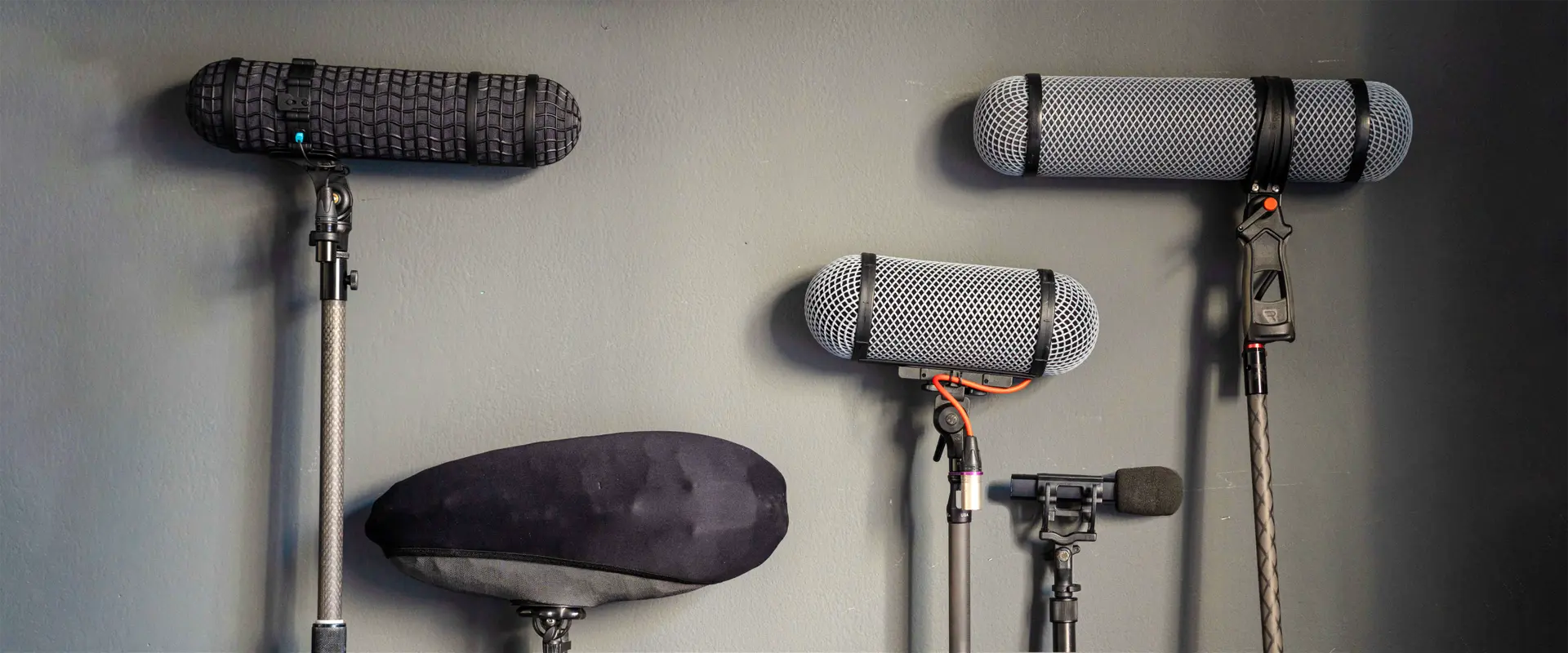 A display of various professional microphone suspensions and shotgun mic shock mounts, including Rycote Lyre models on pistol grips, ready for location sound recording and rental in Italy